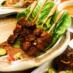 Close-up of flavorful satay skewers served on a lettuce-lined platter with garnishes. Perfect for food enthusiasts.